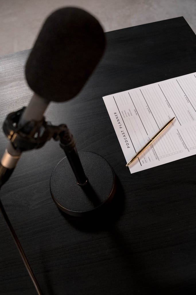 A desk setup featuring a microphone and a podcast planning sheet, perfect for audio recording sessions.