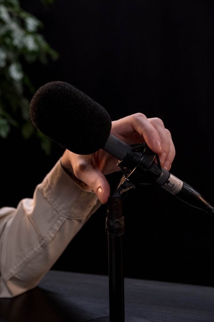 A hand adjusting a microphone stand, ideal for podcast or recording themes.